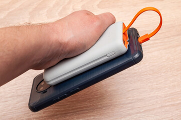 A hand securely grips a phone and power bank connected by an orange cable, ready to charge.