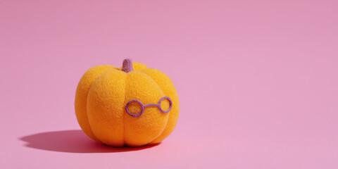 Cute felt pumpkin with tiny glasses on pink background