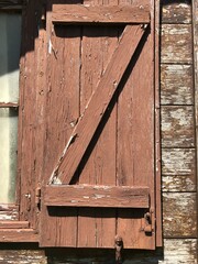 A close-up view of a weathered window shutter, with peeling rustic brown paint, evoking a sense of...