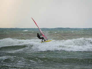 Water Sport Activity - Windsurfer Riding a Wave in Rough Sea on a Windy Day