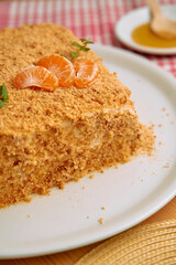 Homemade honey cake with mandarin garnish on white plate and checkered tablecloth