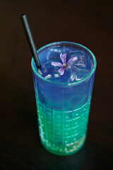 Refreshing blue-curacao cocktail with edible flower and straw in artistic glass