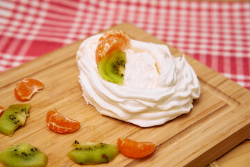Meringue dessert with kiwi and mandarin on wooden board in checkered background