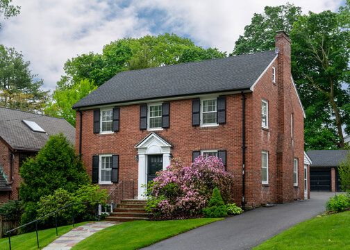Beautiful two-story brick Colonial Revival house with black shutters and flowering bushes in Newton, Massachusetts, USA