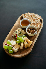 Gourmet cheese platter with grapes crackers honey and nuts on wooden tray