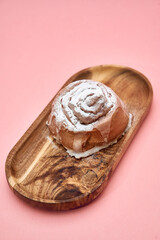 Delicious iced cinnamon roll on wooden serving tray with pink background