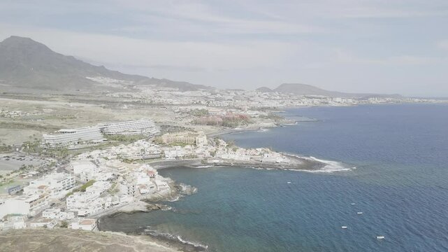 Drone flies south along coast toward Playa El Beril beach on sunny day in Costa Adeje, Tenerife, Canary Islands, Spain