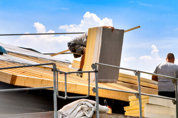 Roofer installing large insulation panels on a roof. Energy-efficient renovation, sustainable...