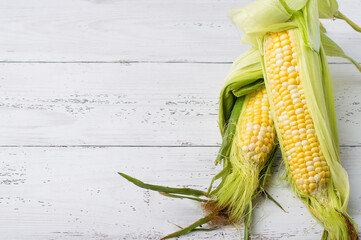 Young cobs of raw corn on a light wooden background, horizontal.