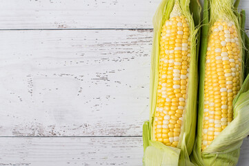 Young cobs of raw corn on a light wooden background, horizontal.