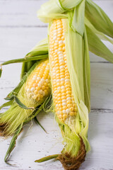 Young cobs of raw corn on a light wooden background.