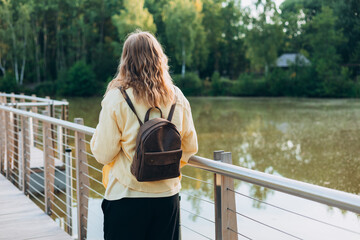 A young happy blonde woman standing on a bridge near a lake on a sunny day. Beautiful morning relax