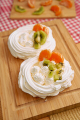 Delicious pavlova dessert with whipped cream, kiwi, and mandarin garnish on wooden board
