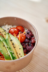 Fresh avocado and bean salad bowl with tomatoes and sesame seeds on light wooden surface