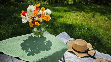 Colorful bouquet of wildflowers in a glass vase on a picnic blanket in sunny green garden. Concept...