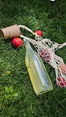 Bottle of lemonade, paper cup and peaches in eco mesh bag on green grass in sunny park. Concept of...