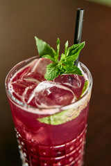 Refreshing iced berry drink with mint garnish in clear glass on dark background