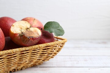 Spoiled apple and good ones in basket on white wooden table, closeup. Space for text