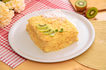 Delicious kiwi-decorated cake on white plate with checkered napkin and flowers