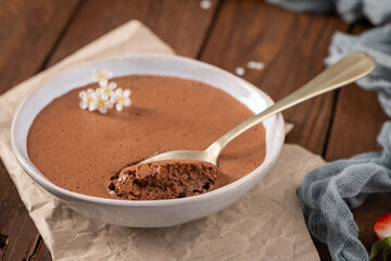 Elegant chocolate mousse in a shallow white dish, a golden spoon scooping a bite, adorned with tiny...