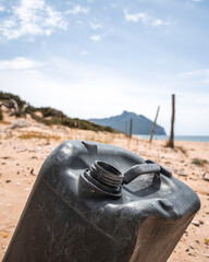 Discarded black plastic container on a sandy beach. The image highlights coastal pollution and...