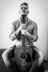 confident man in denim shirt sitting with acoustic guitar in a bold pose, staring upward with determination. A monochrome portrait expressing passion for music and personal identity.