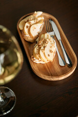 Elegant hors d'oeuvres with pear walnut toast on wooden tray and wine glass