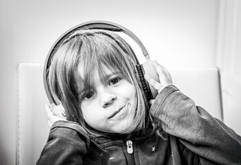 smiling little girl listening to music with big headphones in a playful and relaxed pose. A black and white portrait of joyful childhood and modern tech interaction. Generation alpha concept.