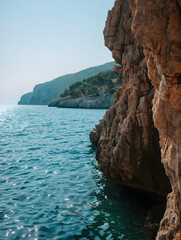 Naklejka premium Photo of sunlight sparkles on the turquoise sea water next to a rugged cliff face