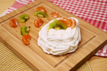 Delicious meringue nest topped with fresh kiwi and clementine slices on wooden board
