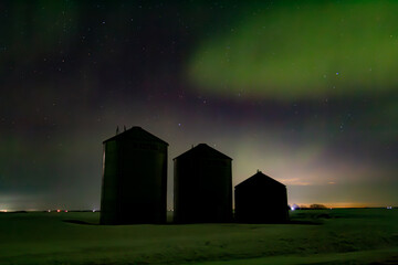 Grain bins silhouetted by night sky and aurora