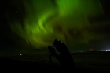 person under night aurora sky with telescope