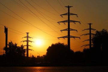 Silhouettes of high voltage towers with electrical wires on background of sunset sky. Electricity...