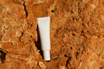 White mockup tube of serum or face cream on limestone rock on the beach. Concept of natural skin...