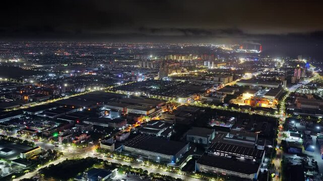 Aerial shot of a sprawling industrial zone and cityscape illuminated at night in a modern Asian city.