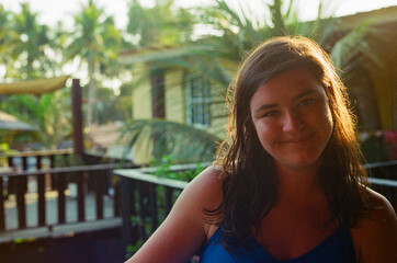 A cheerful woman enjoying a sunny day outdoors with lush tropical trees and wooden railings in the background, showcasing a warm and inviting atmosphere.