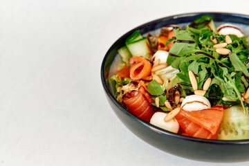 Fresh salmon salad with arugula, pine nuts, and mozzarella in black bowl