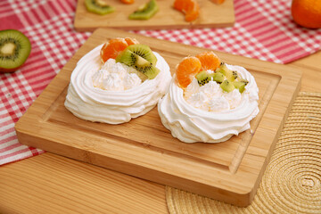 Delicious kiwi and mandarin pavlova on wooden tray with red checkered napkin