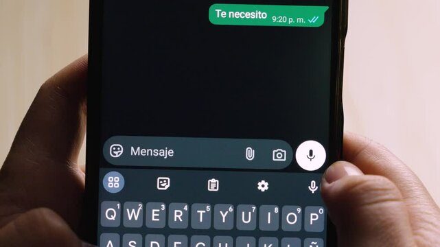 Close-up of hands composing a Spanish text message on a phone that reads "Te necesito" (I need you).