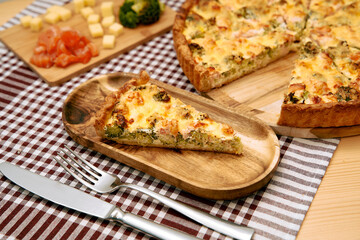 Savory broccoli and cheese quiche slice on wooden plate with knife and fork on checked tablecloth