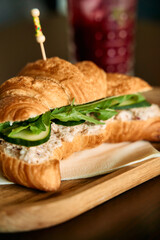 Delicious croissant sandwich with tuna salad avocado and fresh greens on wooden board