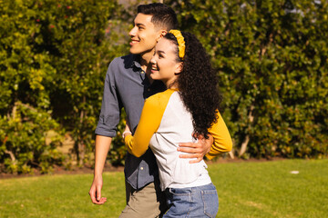 Diverse couple hugging and smiling on grassy lawn by green hedge wearing yellow headband