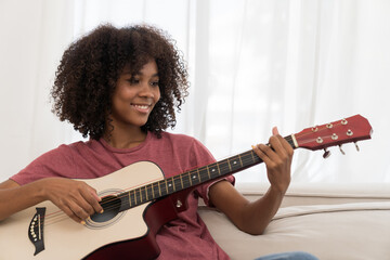 Music, woman and playing guitar for song. African American woman playing guitar on sofa in living...