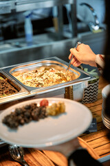 Buffet dining experience: person serving from stainless steel chafing dish