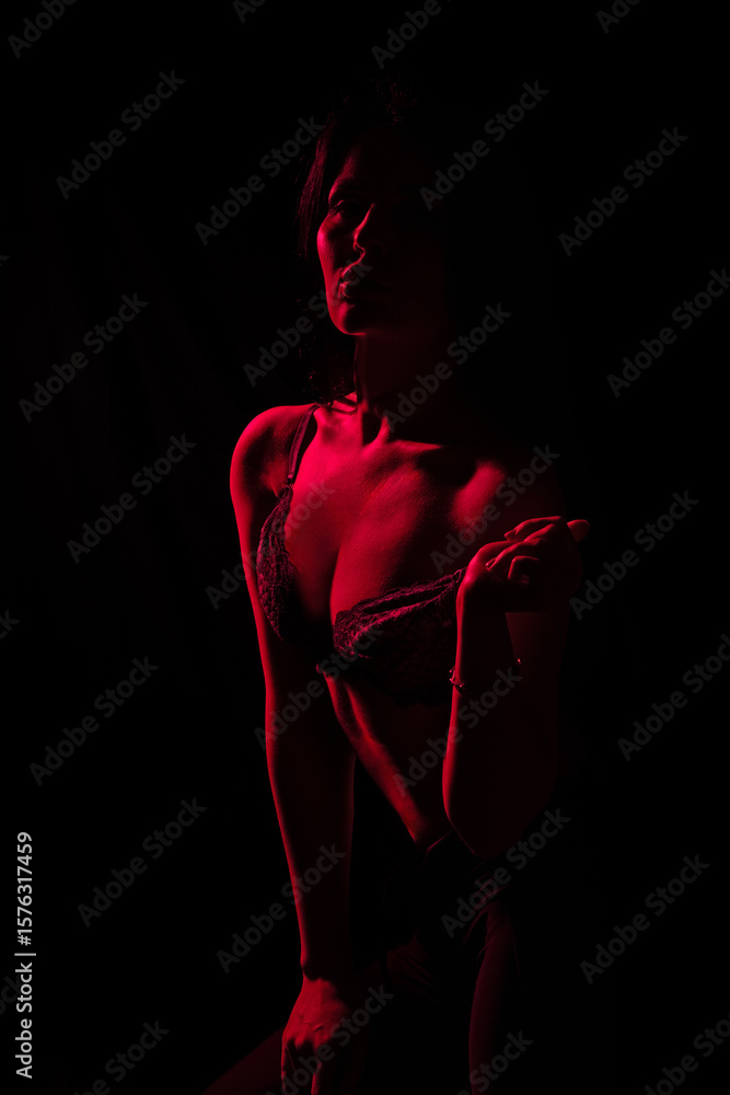 Poster model strikes a confident pose in a dark setting illuminated by red light, emphasizing her silhouett