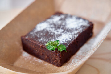 Delicious chocolate brownie with mint garnish and powdered sugar on craft paper tray