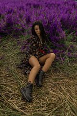 Brunette woman sits gracefully in field filled with blooming delphiniums Bright flowers surround...
