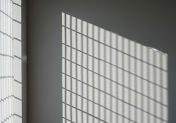 A pristine, minimalist light grey wall with strong, sharp geometric shadows from a rectangular window and vertical blinds, creating a bright copy space area. Concept of architectural light and shadow