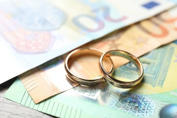 Gold wedding rings and euro banknotes on wooden table, closeup