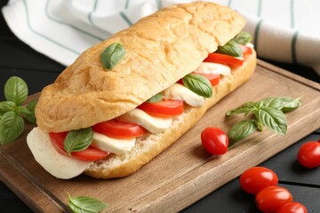 Tasty sandwich with mozzarella cheese, tomatoes and basil on black wooden table, closeup